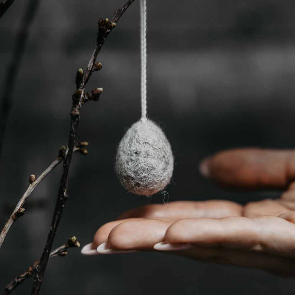 Eine Hand hält einen Storefactory - Ullas Ei Anhänger auf einem Ast.