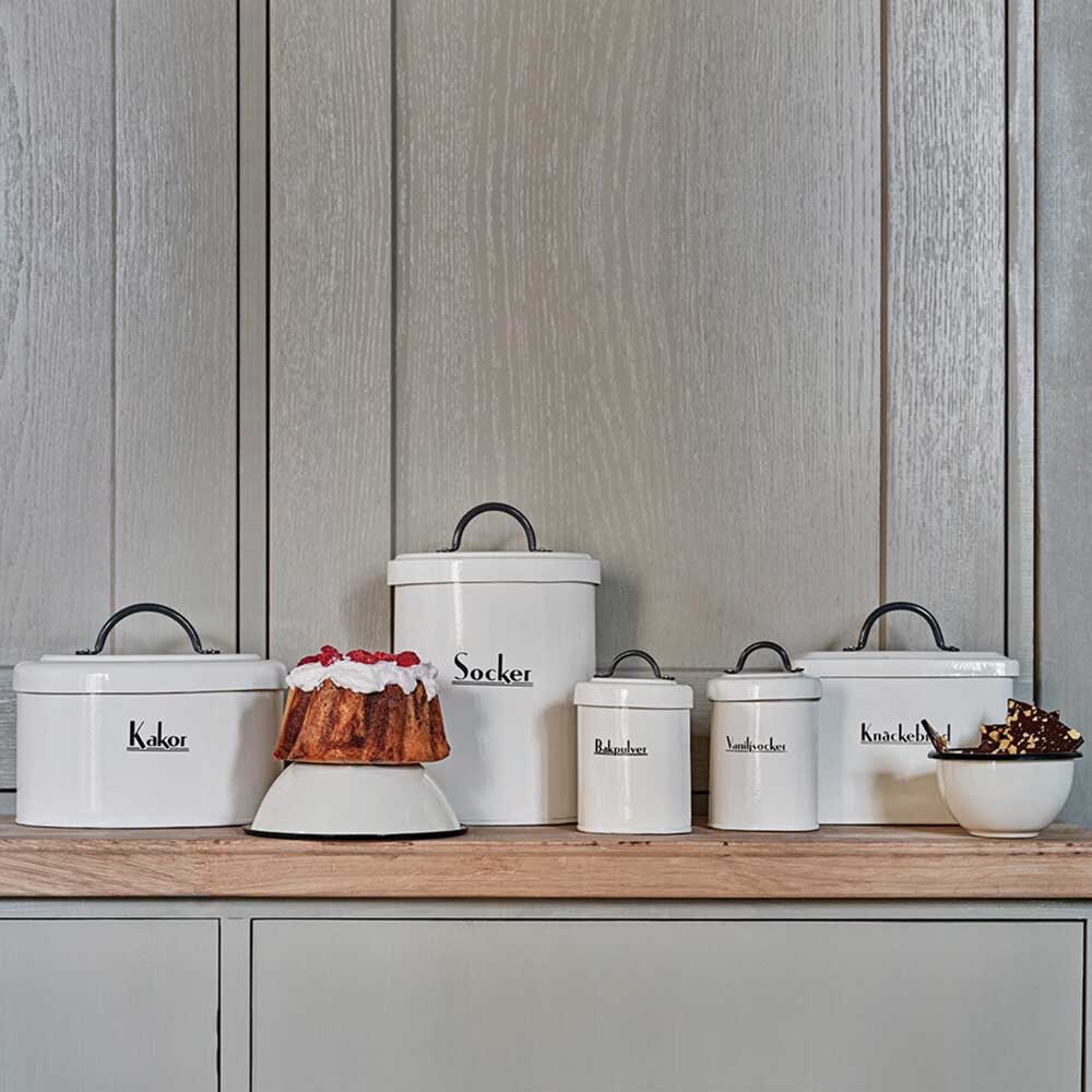 Weiße Vorratsbehälter für die Küche von Strömshaga mit schwedischen Etiketten, die verschiedene Süßigkeiten und Zutaten auf einer Holzarbeitsplatte präsentieren.