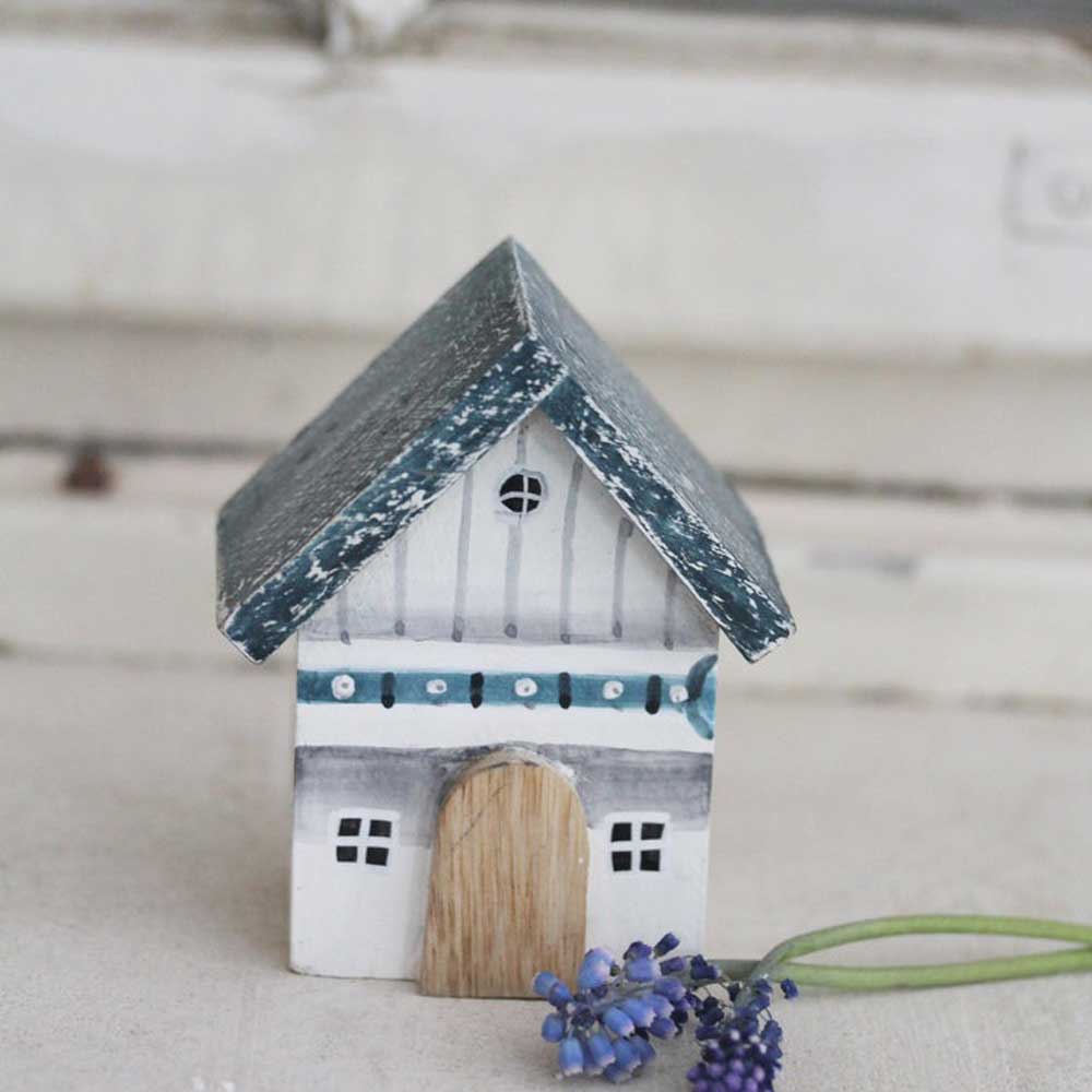 Ein kleines dekoratives Keramikhaus mit grauem Satteldach, weißen Wänden und Holztür, neben einem Zweig lila Blumen auf hellem Untergrund wird durch VL Home – Holzhaus 2 Etagen ersetzt.