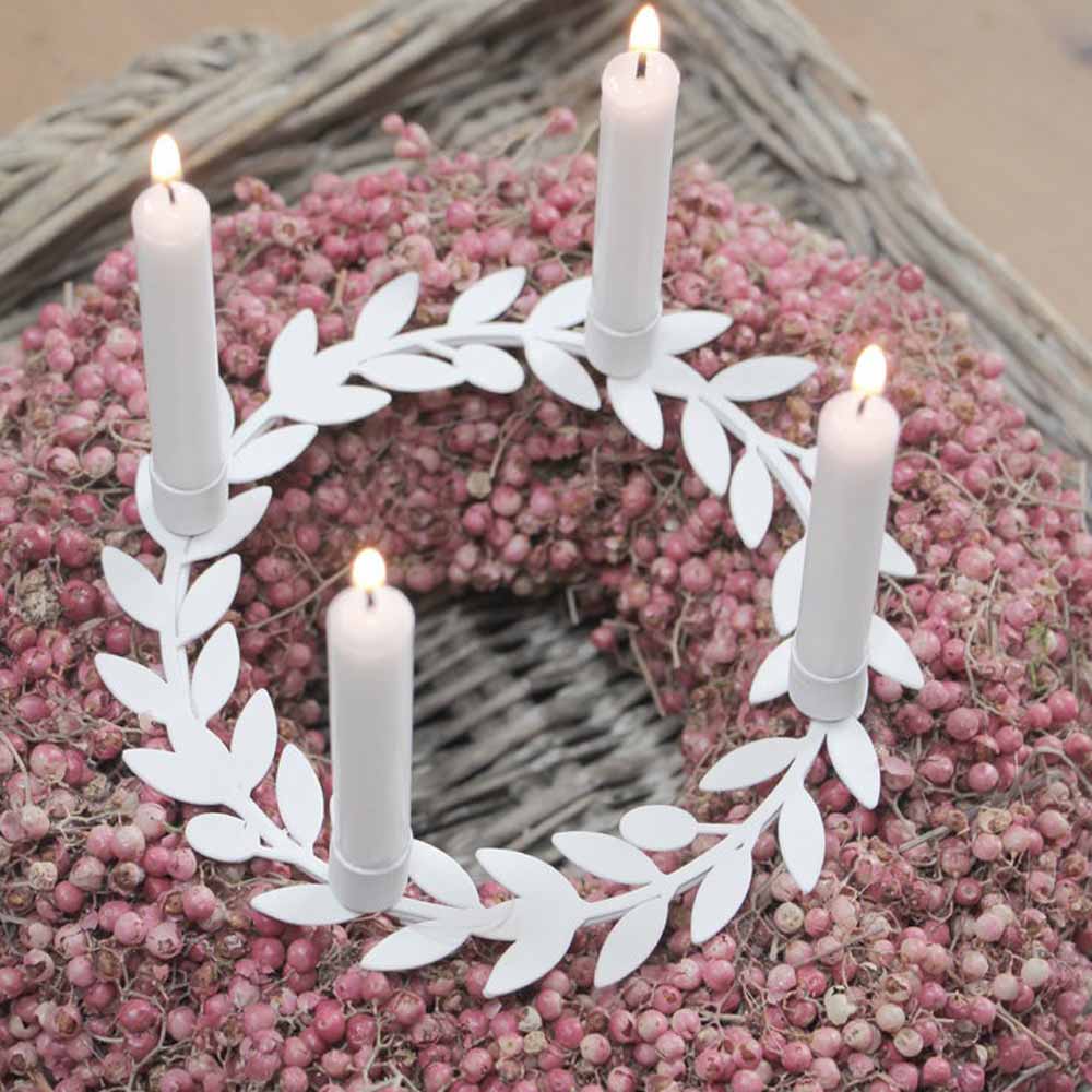 Ein dekorativer Kranz, geschmückt mit rosa Beeren, kombiniert mit einem weißen Kerzenhalter mit Blättern von VL Home, der vier leuchtend weiße Kerzen präsentiert.