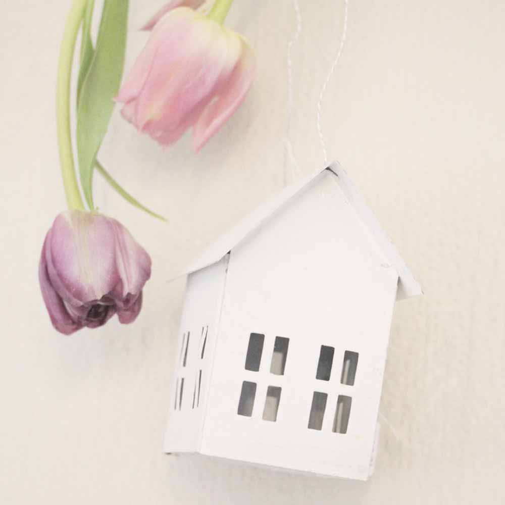 Eine kleine VL Home – Metallhaus Deko zum Hängen hängt neben verwelkten rosa Tulpen vor hellem Hintergrund.