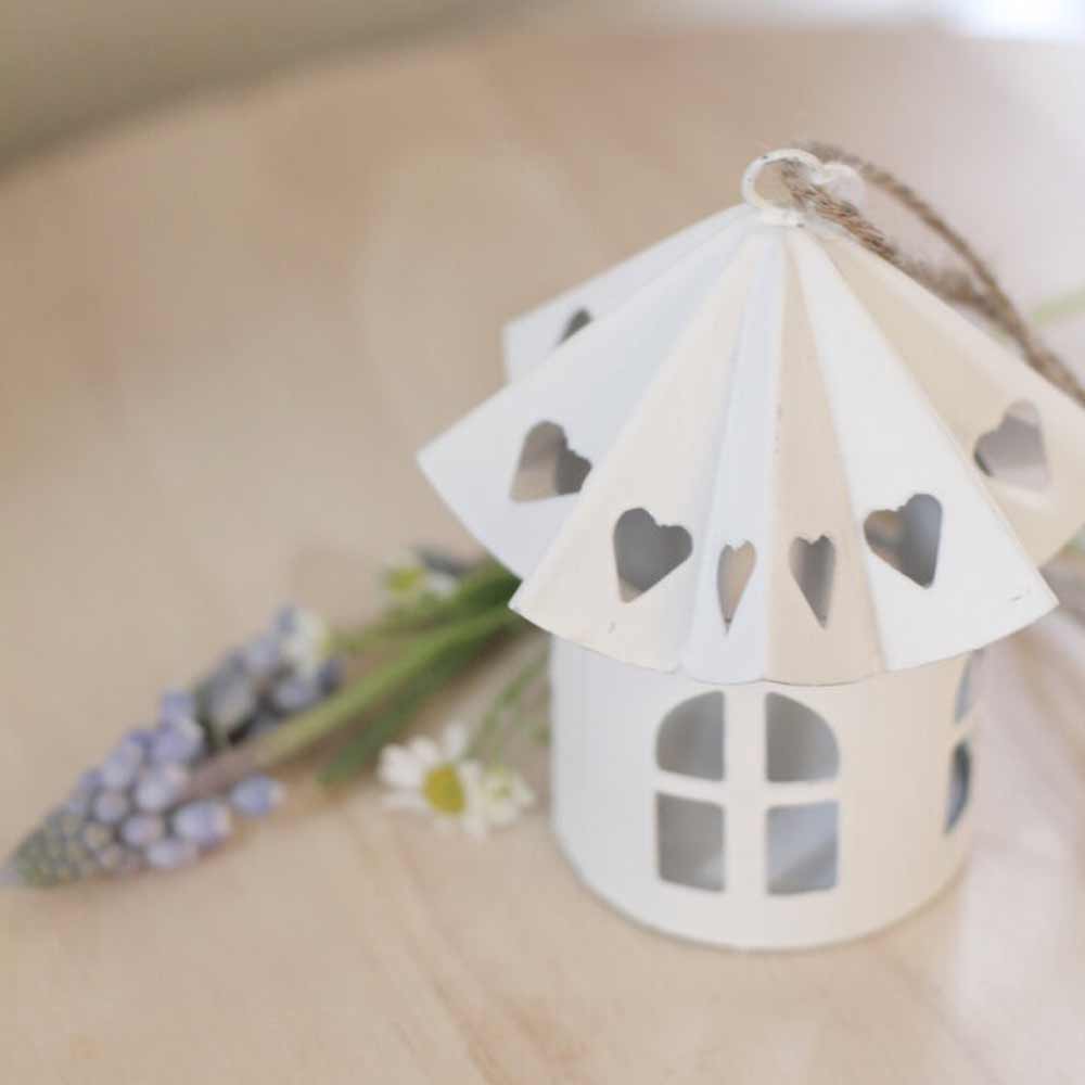 Das VL Home – Vogelhaus Metall rund mit Herzen im Dach, ein kleines Dekohaus aus weißem Metall mit herzförmigen Dachausschnitten, steht auf einem hellen Holzuntergrund neben Lavendel und kleinen weißen Blumen.
