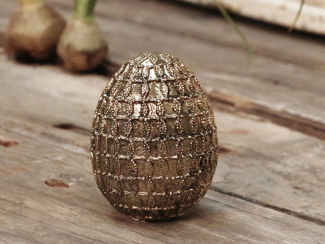 Ein Chic Antique - Osterei Vintage Gold mit Pailletten mittelgroß auf einer Holzoberfläche.