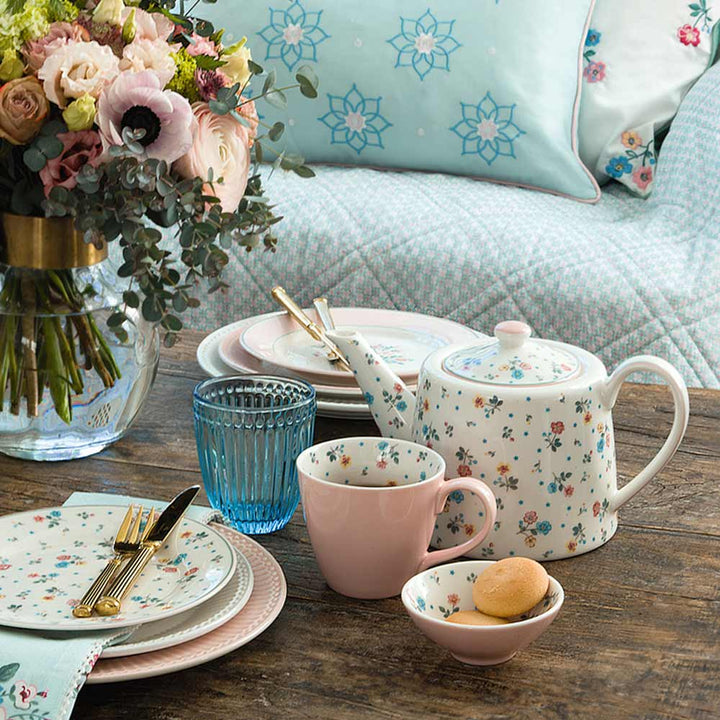 Elegante Tischdekoration mit Teeservice mit Blumenmuster, weißem Geschirr von GreenGate - Adelena Frühstücksteller, goldenem Besteck und einem Blumenstrauß in einer klaren Vase, bereit für einen Nachmittagstee.