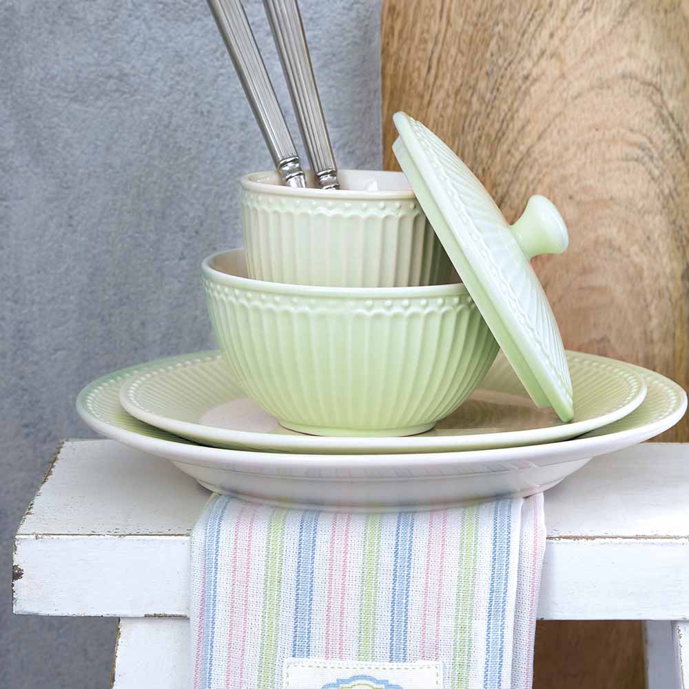 Gestapelte GreenGate - Alice Latte Tassen und Schüsseln mit Utensil, auf einem weißen Holzhocker mit gestreiftem Tuch.