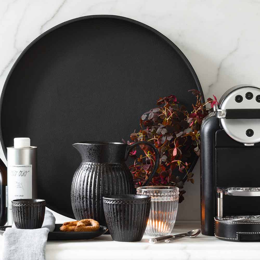Eine stilvolle Küchentheke mit einer schwarzen Espressomaschine, dazu passender Keramiktöpferei, Gläsern und einer GreenGate - Alice Servierplatte vor einem Marmorhintergrund.