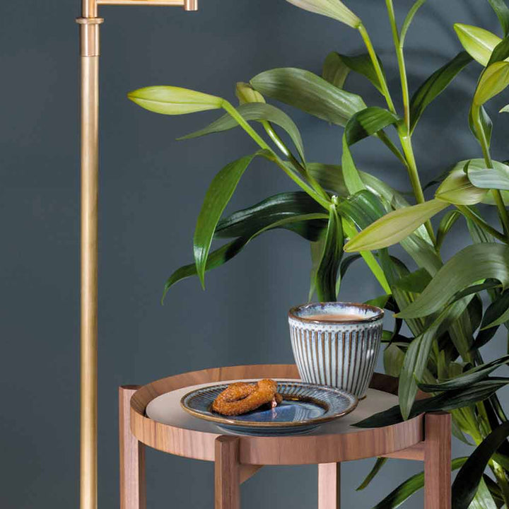 Ein kleiner Holztisch mit einer GreenGate - Alice Servierplatte, auf der Kroketten liegen, neben einer großen Pflanze und einer Messing-Stehlampe vor einer grauen Wand.