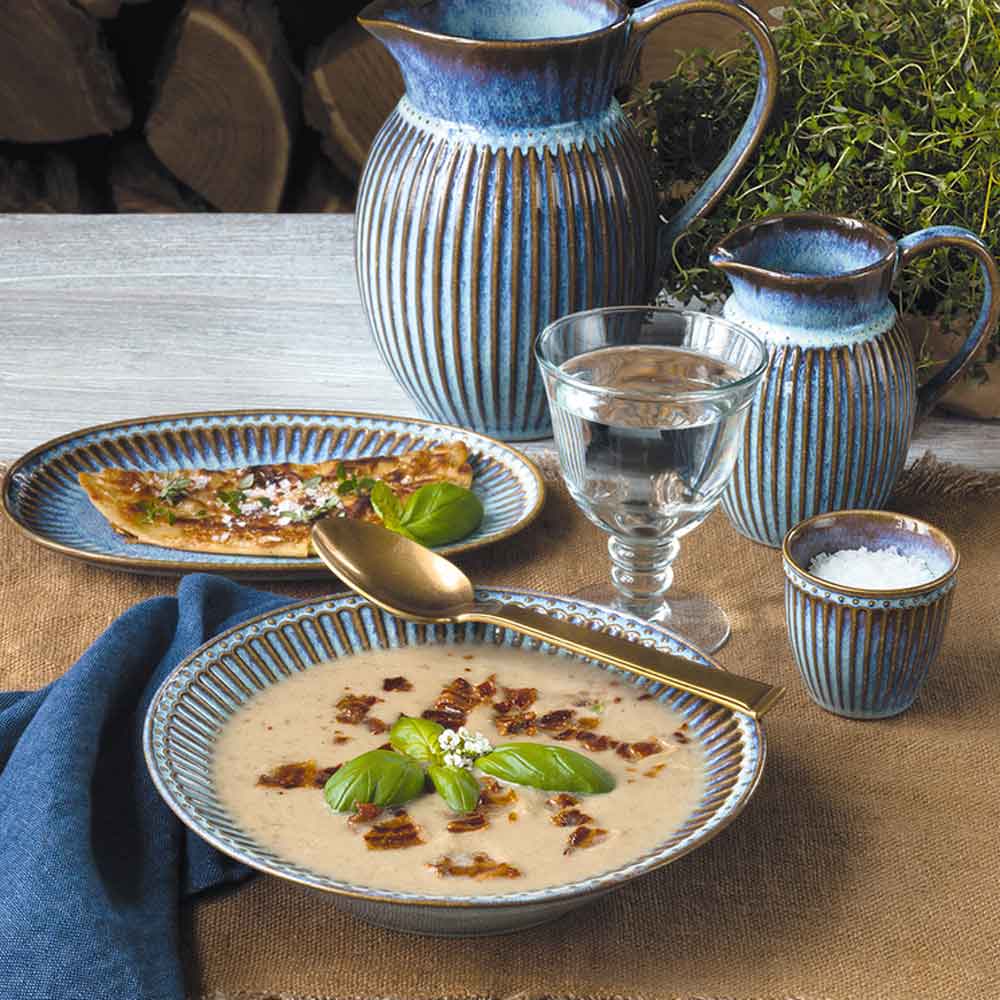 Ein rustikaler Tisch mit einer Schüssel cremiger Suppe, garniert mit Basilikum, einem Glas Wasser und einer GreenGate - Alice Teekanne.