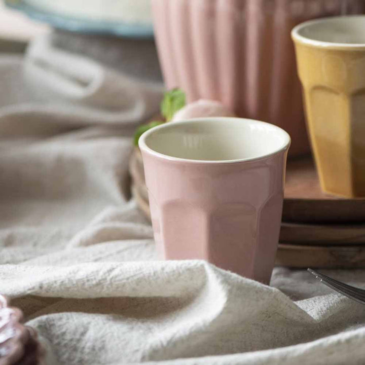Ein rosa Ib Laursen - Cafe Latte Becher Mynte auf einem strukturierten Tuch, mit anderen Keramikbechern und einem weichen Hintergrund.