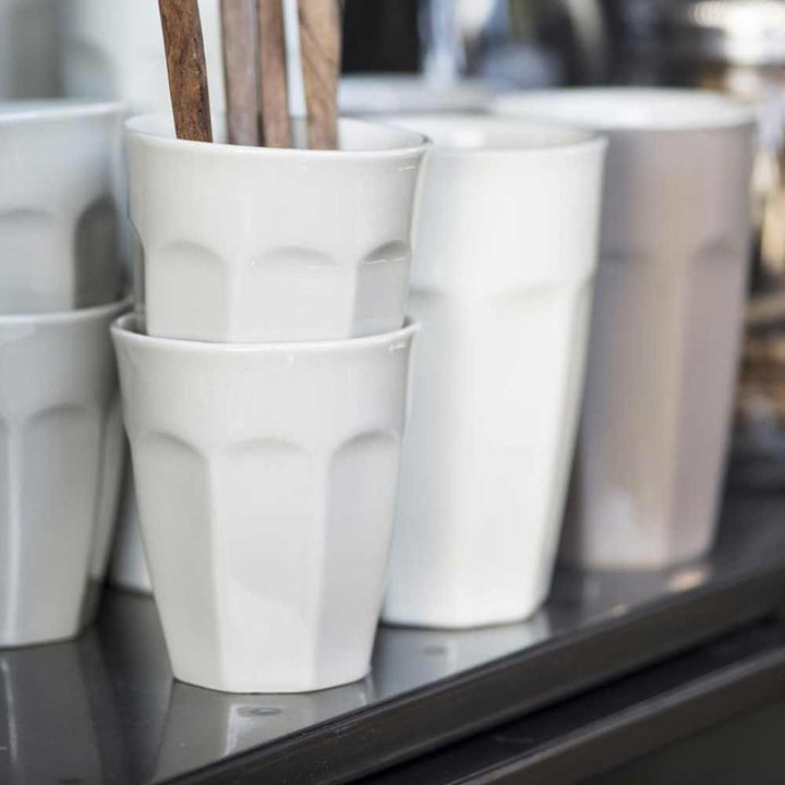 Eine Reihe von Ib Laursen - Cafe Latte Becher Mynte-Tassen und Utensilien auf einem Regal, wobei der Fokus auf dem strukturierten Design der jeweils nächsten Tasse liegt.