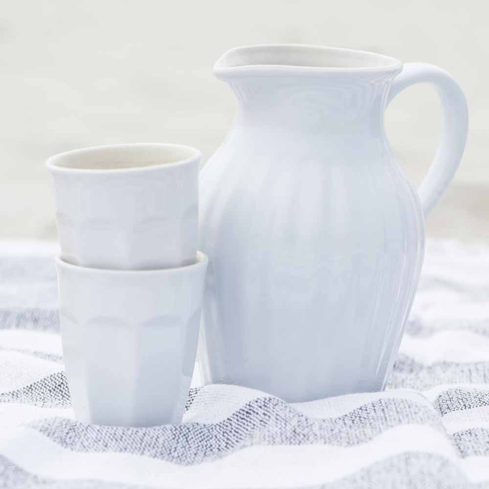 Ein weißer Ib Laursen - Cafe Latte Becher Mynte aus Keramik und zwei Tassen auf einem strukturierten Tuch mit einem weichen, unscharfen Hintergrund.