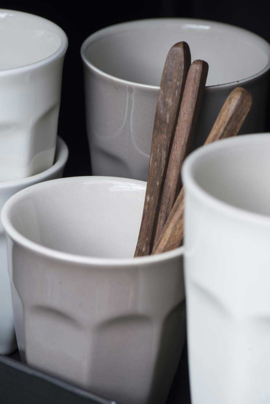 Gestapelte Ib Laursen - Cafe Latte Becher Mynte-Tassen in gedeckten Tönen mit Holzlöffeln darin, vor einem dunklen Hintergrund.