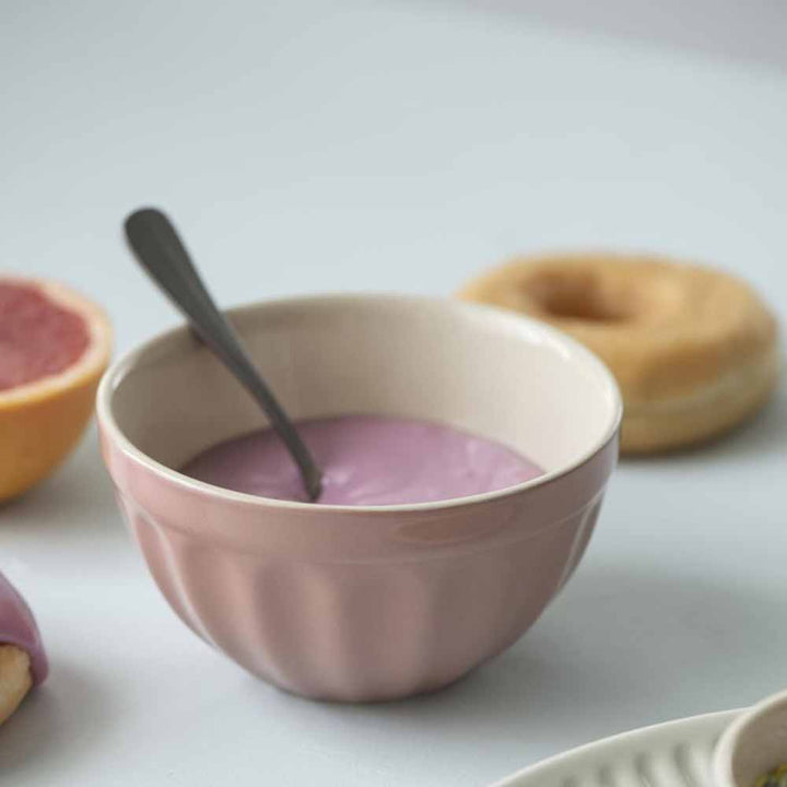 Eine Ib Laursen - Müslischale Mynte aus rosa Joghurt mit Löffel, umgeben von einer halbierten Grapefruit und Donuts auf hellem Hintergrund.
