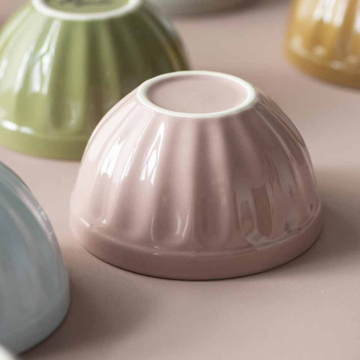 Nahaufnahme einer Ib Laursen - Müslischale Mynte in hellrosa Keramikschale mit geriffeltem Design, umgeben von weiteren pastellfarbenen Keramikschalen.