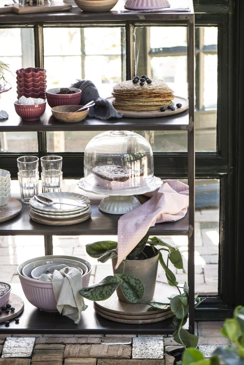Eine ordentlich arrangierte Ib Laursen – Tortenplatte Mynte mit Küchenutensilien, Backwaren und einer Topfpflanze am Fenster.