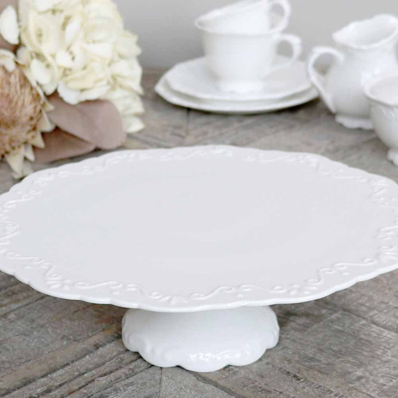 Chic Antique Tortenplatte Provence in Weiss mit Reliefrand auf grauem Altholz, dahinter weisses Geschirr und Hortensien