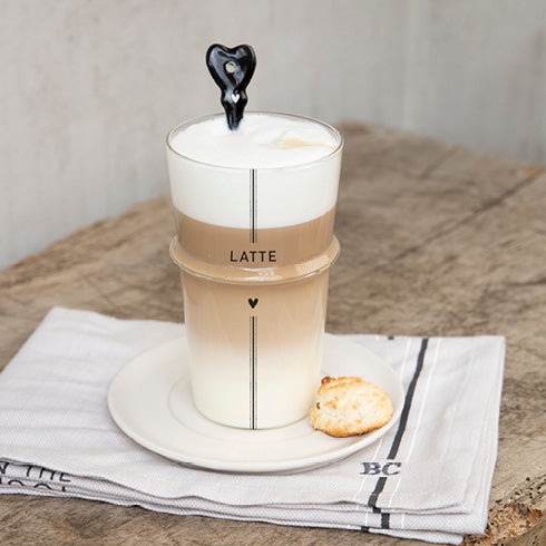Eine Tasse Bastion Collections - Löffel für Latte Macchiato Herz schwarz mit einem Keks darauf.