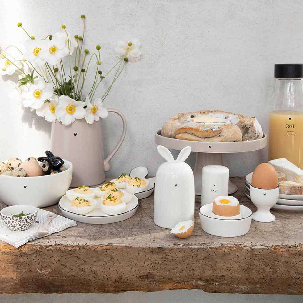 Ein Tisch voller Teller, Schüsseln, Tassen und Bastion Collections – Eierwärmer Keramik Hase weiß.