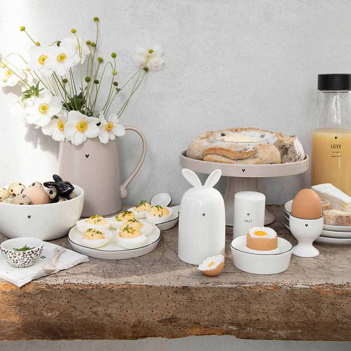 Ein Tisch voller Teller, Schüsseln, Tassen und Bastion Collections – Eierwärmer Keramik Hase weiß.
