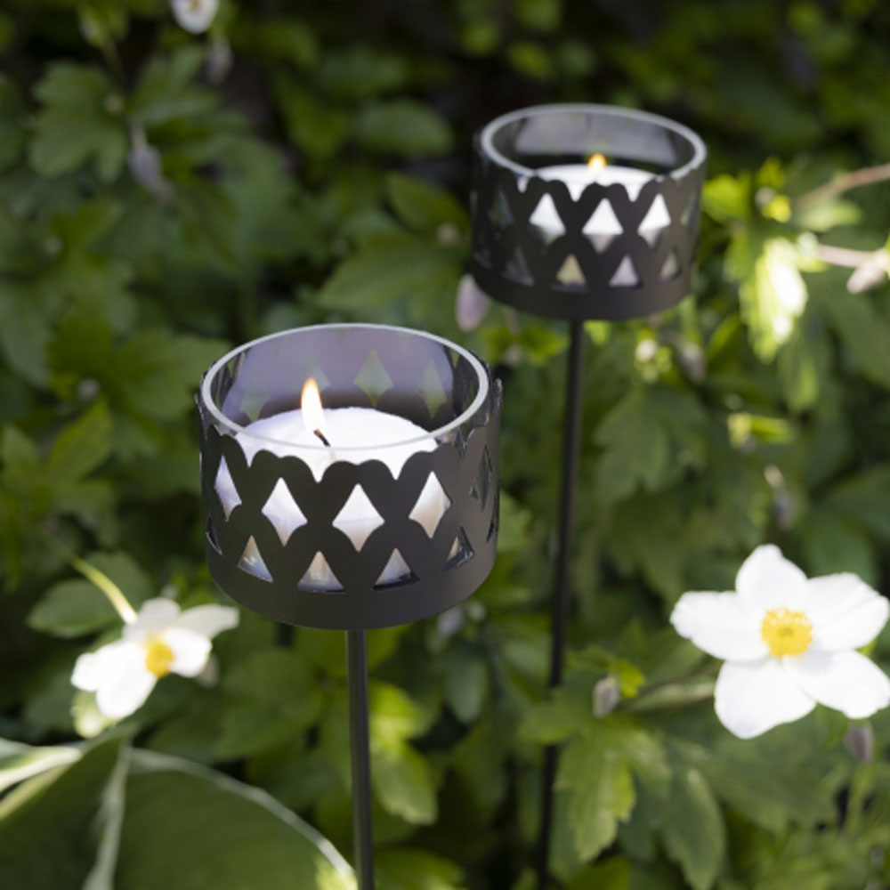 Zwei Bastion-Kollektionen – Gartenlicht Teelichthalter mit Spieß in einem Garten mit weißen Blumen.