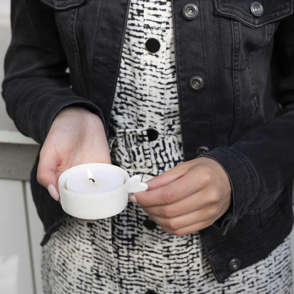 Eine Frau hält einen Bastion Collections – Kerzenhalter mit Herzhenkel weiß in einer Jacke.