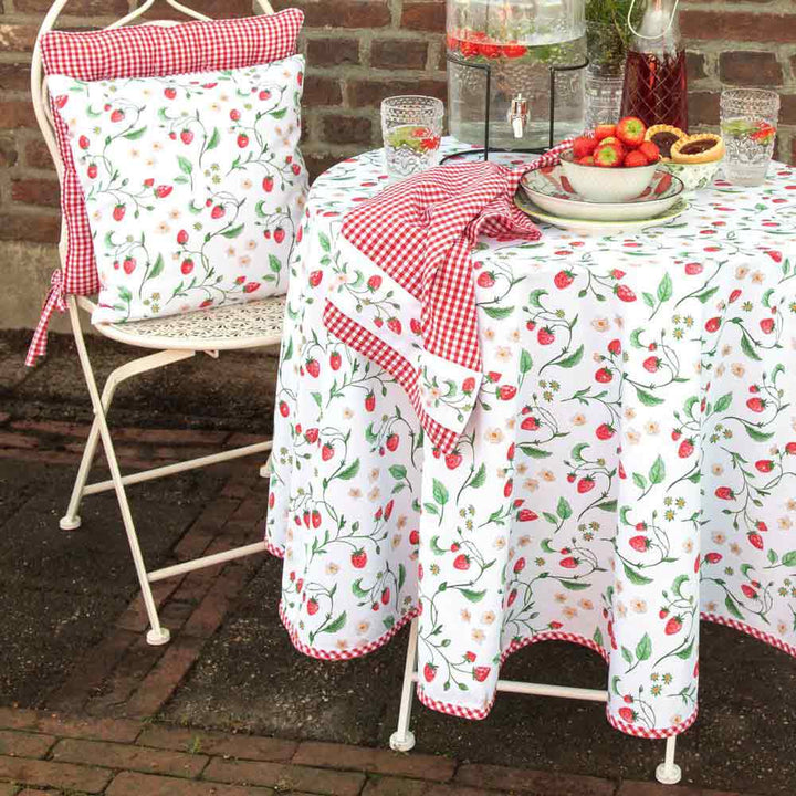 Essplatz im Freien mit einem weißen Stuhl und einem mit einer Tischdecke von Clayre & Eef – Tischläufer Strawberry Länge: 140 cm bedeckten Tisch, komplett mit Tellern und Gläsern auf einer gemauerten Terrasse.