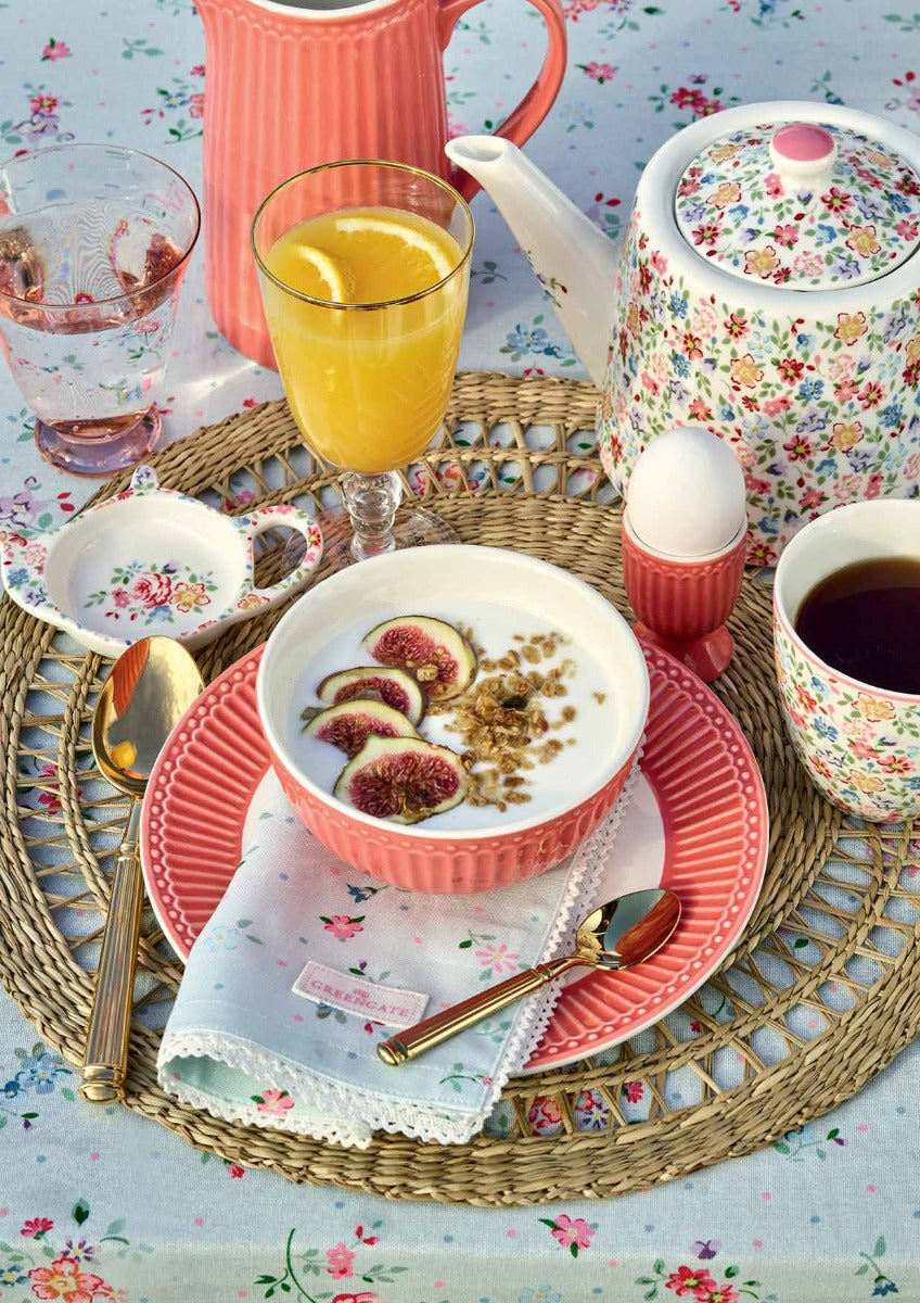 Ein Frühstücksgedeck auf einer hellblauen Tischdecke vom Typ GreenGate - Belle Stoffserviette mit Spitze mit Joghurt mit Feigen, einem weichgekochten Ei, Tassen Tee und einem Krug Saft.