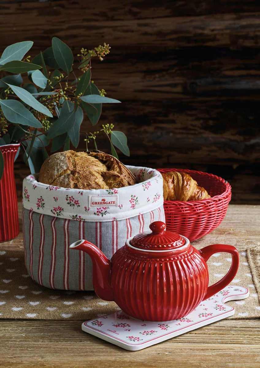 Eine rote Teekanne auf einem Tablett neben einem mittelgroßen weißen GreenGate - Alice Brotkorb mit frischem Brot und Croissants vor einem rustikalen Holzhintergrund.