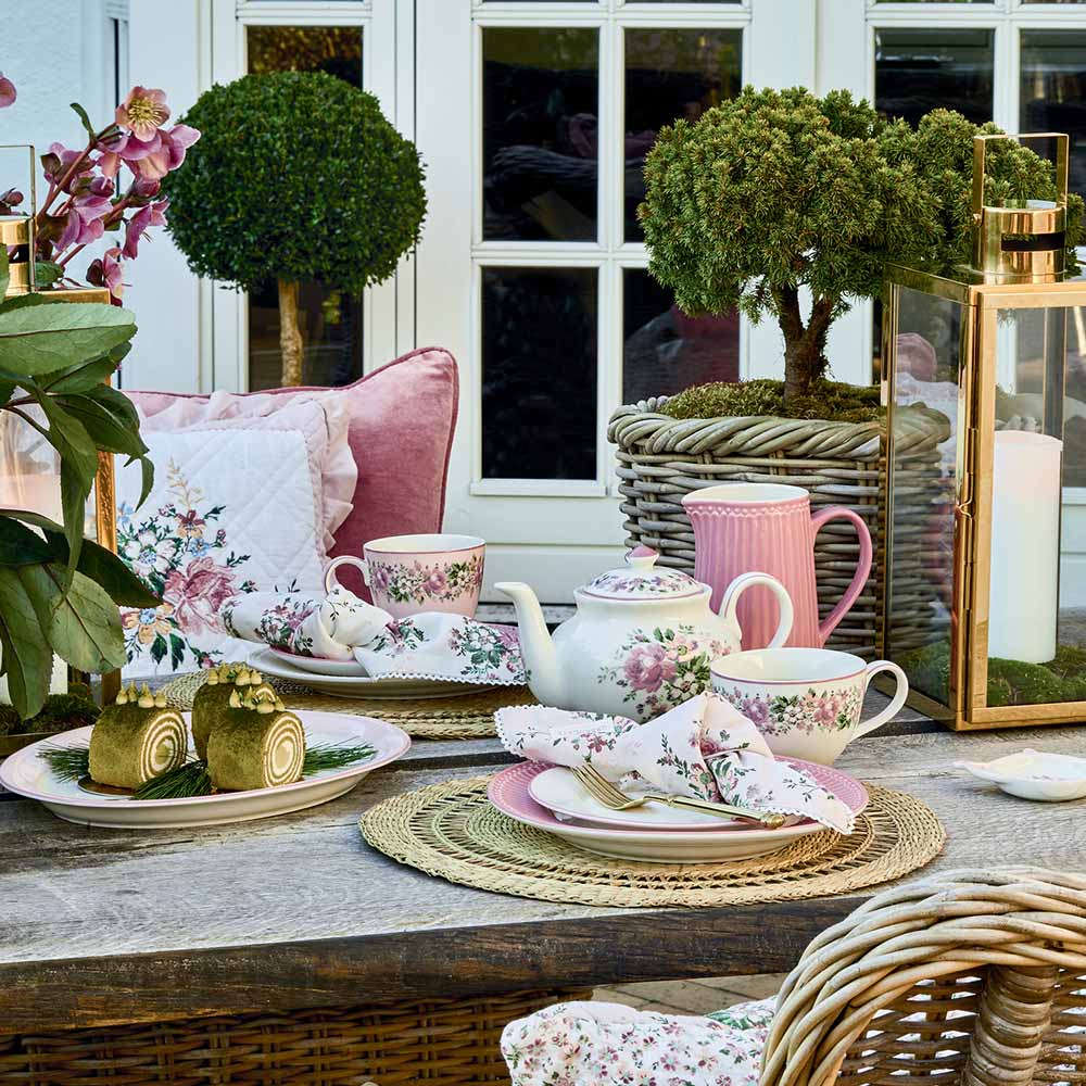 Landhaustisch mit floraler GreenGate-Tischwäsche, rosa Geschirr und Stühlen aus Geflecht