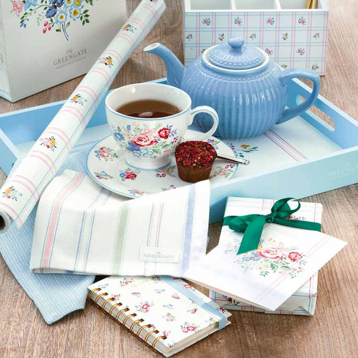 Ein gemütliches Tee-Set mit einer weißen Teekanne, einer Tasse Tee und floralen Schreibwarenartikeln vom GreenGate - Gaby Besteckkasten auf einem hellblauen Tablett.