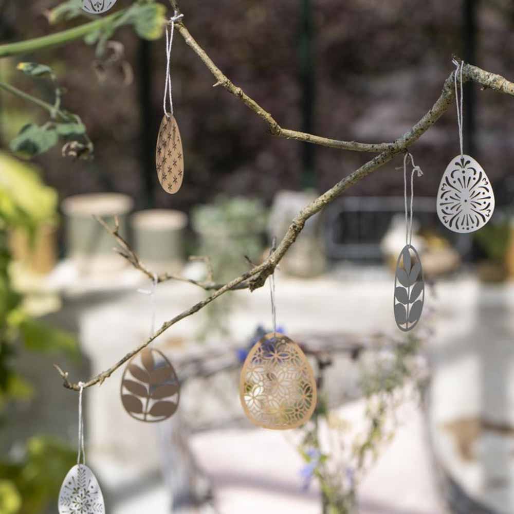 Dekorative Eier von Ib Laursen – Scherenschnitt Ei Blumenmuster, die an einem Ast in einer Gartenumgebung hängen.