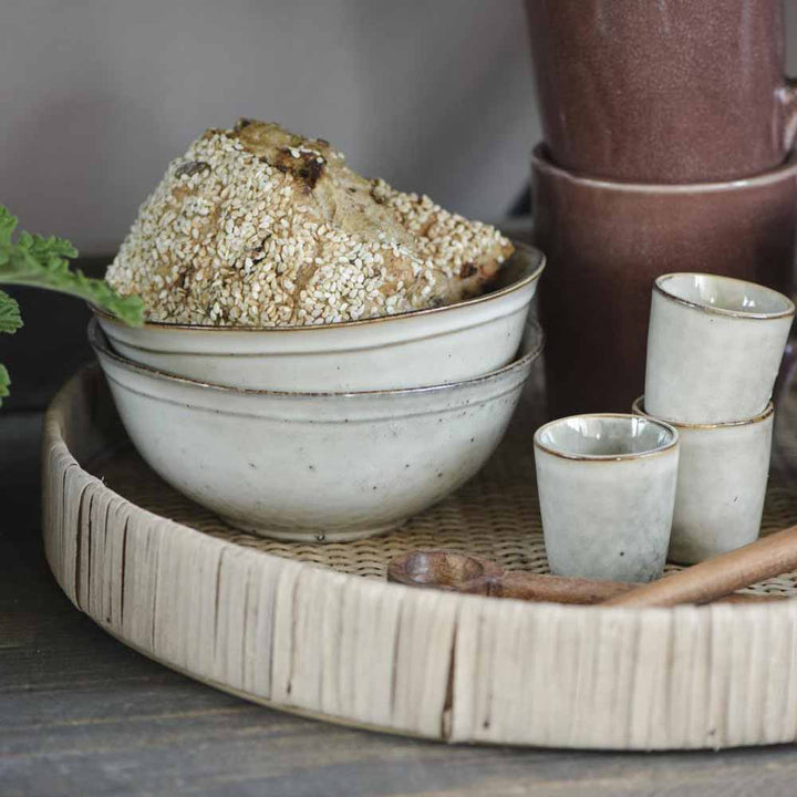 Eine Keramikschüssel mit sesamummanteltem Brot, dazu zwei Ib Laursen - Eierbecher Sand Dunes und eine braune Kanne auf einem geflochtenen Tablett.