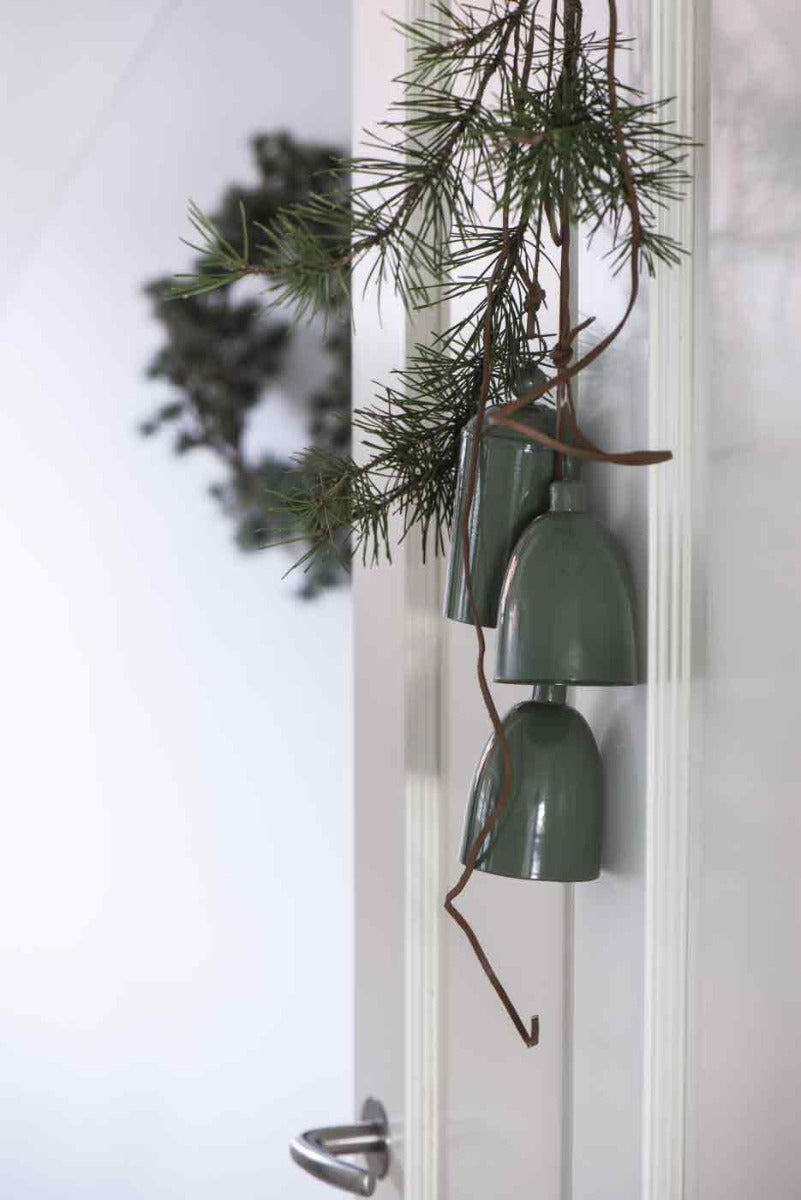 Drei Ib Laursen - Glocken konisch grün hängen an einem Tannenzweig mit unscharfem Fensterhintergrund.