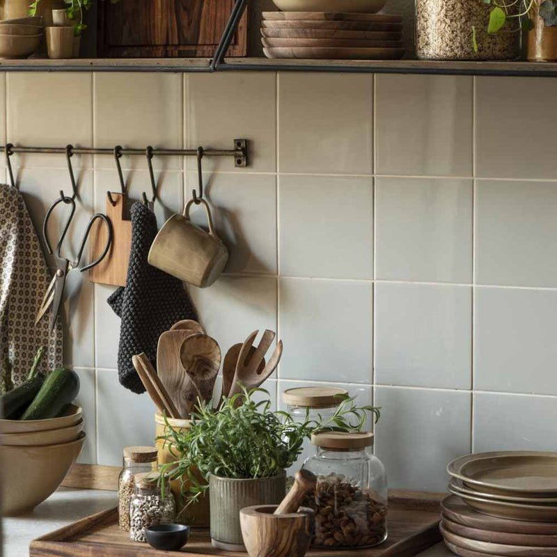 Küchenarbeitsfläche mit Holzbesteck, Kräutern und Keramik vor hellen Fliesen