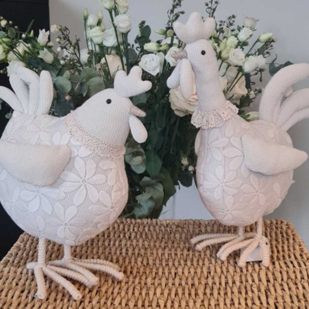 Zwei La Galleria - Huhn mit Blumenspitze kurze Beine cremeweiß auf einer gewebten Matte mit einem Blumenarrangement im Hintergrund.