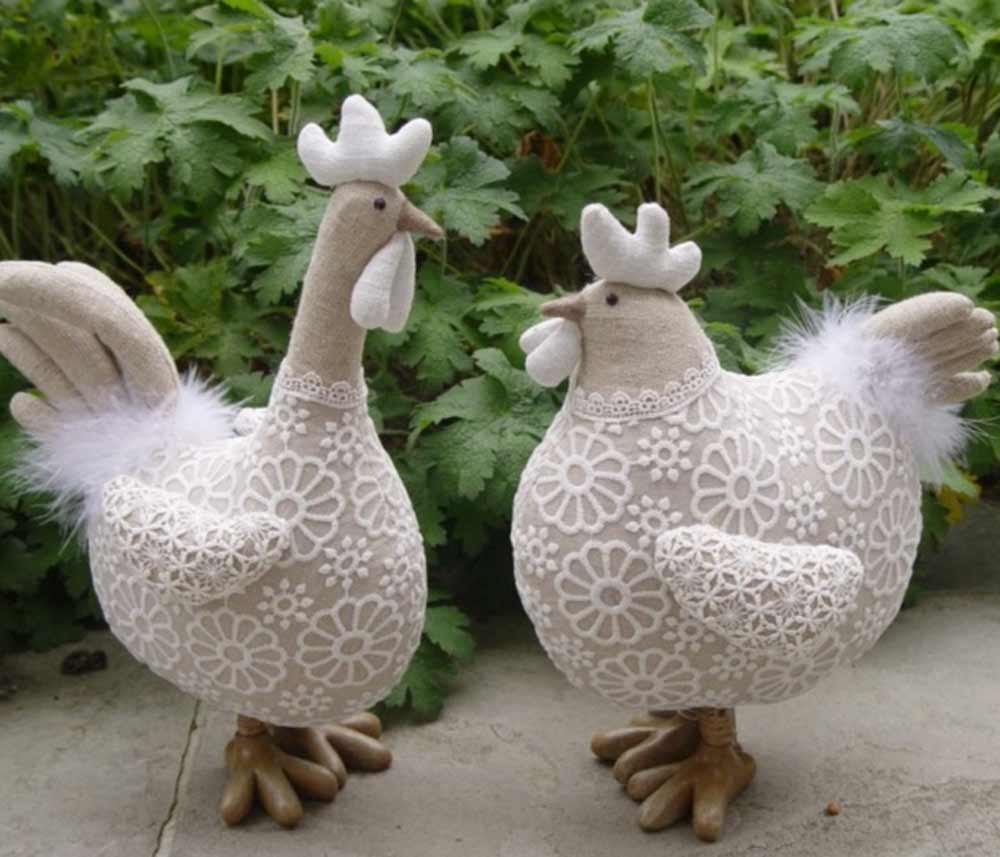 Zwei La Galleria - Huhn mit Blumenspitze kurze Beine weiße Figuren mit Spitzenmuster vor grünem Blattwerk.