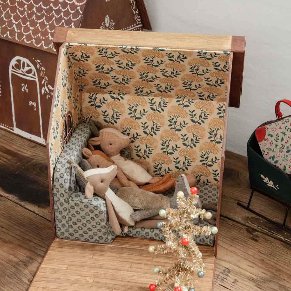 Eine Maileg - Hirsch Little Sister, offen auf dem Boden, mit gemusterter Innenseite, die zwei Plüschtiere und einen kleinen dekorativen Weihnachtsbaum enthält.