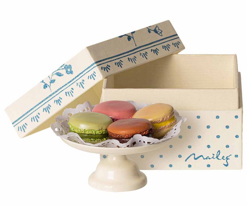 Eine Auswahl an Maileg – Macarons et Chocolat Chaud, präsentiert auf einem kleinen Podest neben der offenen Schachtel.