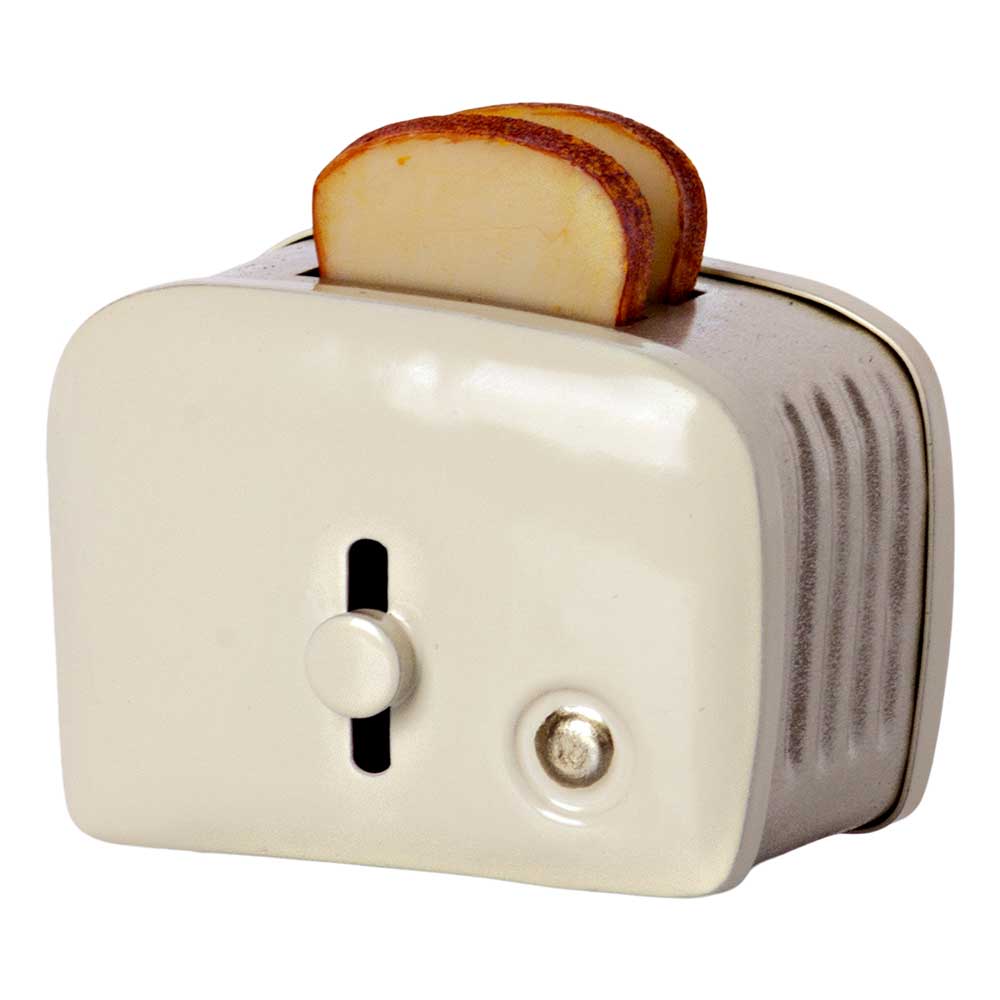 Ein Apfelstück liegt auf einem Maileg – Puppenhaus Toaster mit Toast weiß mit einem Zifferblatt an der Seite.