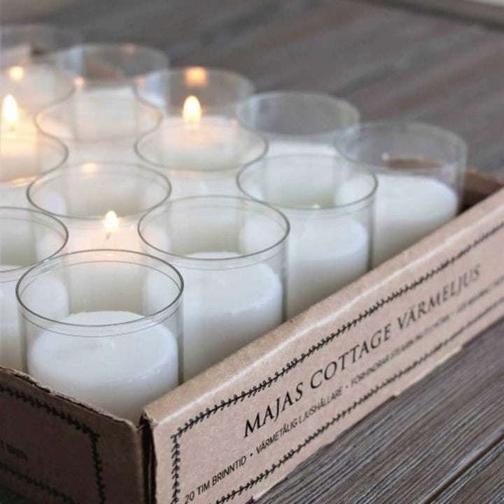Eine Schachtel Majas Cottage - Teelicht-Duftkerzen mit mehreren brennenden Kerzen, präsentiert auf einer Holzoberfläche.