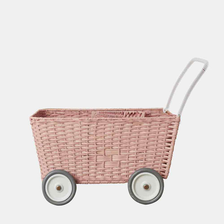 Ein Olli Ella - Puppenwagen Strolley rosa auf Rädern mit weißem Griff, isoliert auf hellem Hintergrund.
