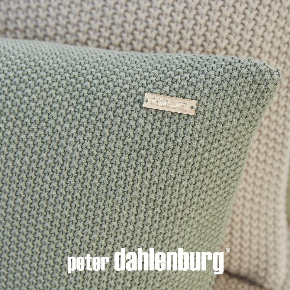 Nahaufnahme eines grün strukturierten Strickkissenbezugs mit Perlen-Reiskornmuster und Salbei mit einem kleinen, rechteckigen Etikett mit der Marke Peter Dahlenburg.