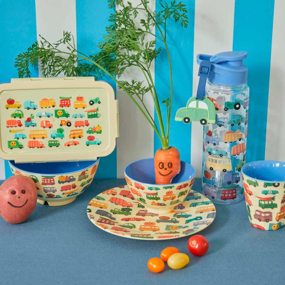 Kinder-Menüset mit Rice - Melaminteller „Happy Cars“, bestehend aus Tellern, Schüssel, Wasserflasche und Lunchbox auf blau gestreiftem Hintergrund, mit einer lächelnden Karotte und bunten Süßigkeiten.
