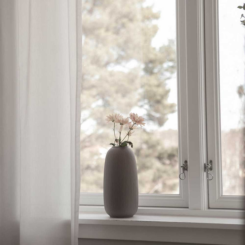 Braune Vase mit hellen Blüten auf einer weißen Fensterbank