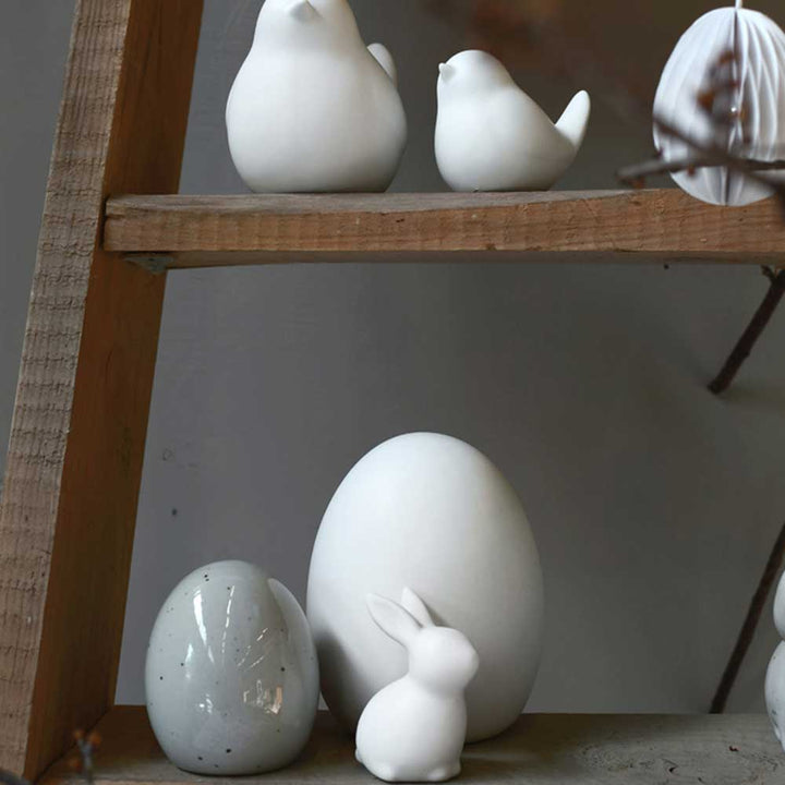 Storefactory – Bjuv Ei Keramik-Dekorationen, darunter Vogel- und Hasenfiguren und verschiedene Eierformen, ausgestellt auf Holzregalen.