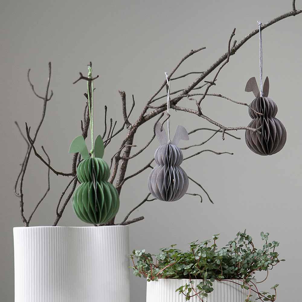 Three Storefactory - Hilma Anhänger Osterhase Papier braun gestaltet, um wie Ostereier auszusehen, die an einem kahlen Ast hängen, mit einer Topfpflanze im Vordergrund.