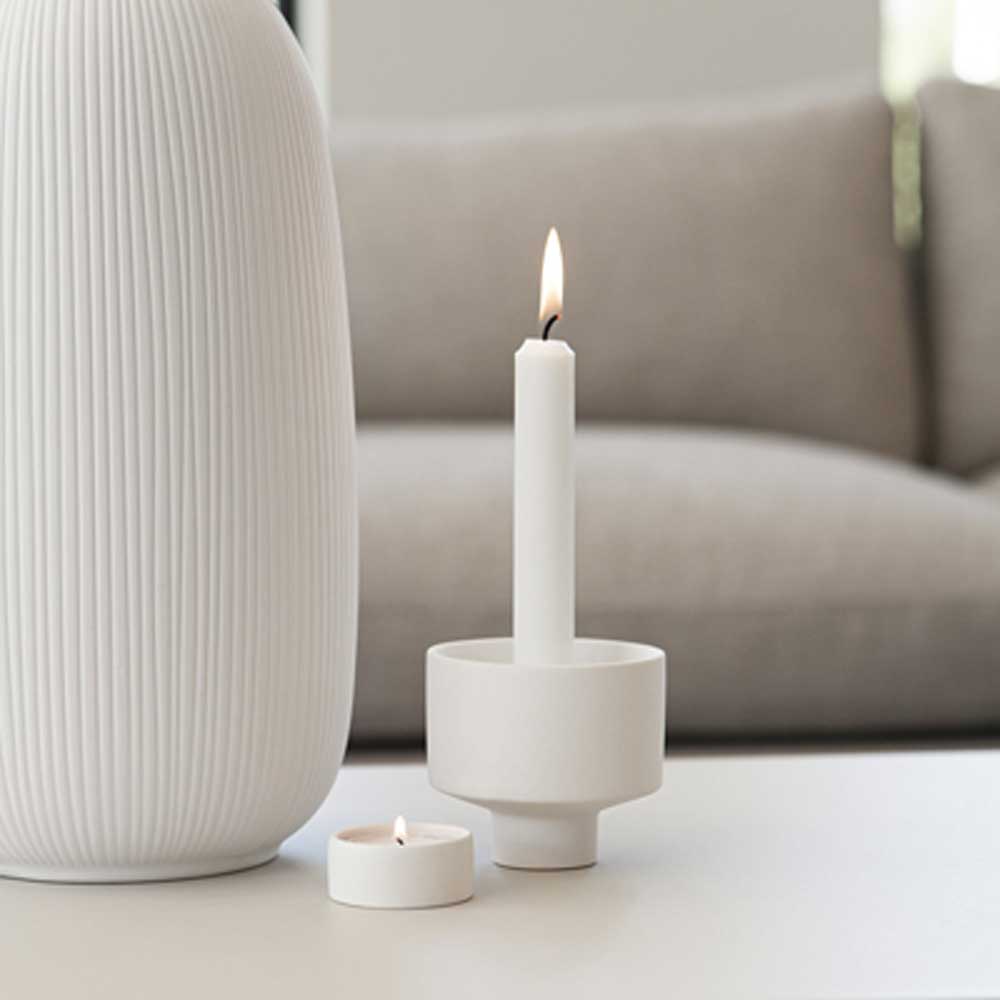 Ein Storefactory - Liaved Kerzenhalter für Stabkerzen und Teelicht weiß sitzt auf einem Tisch neben einer Kerze.