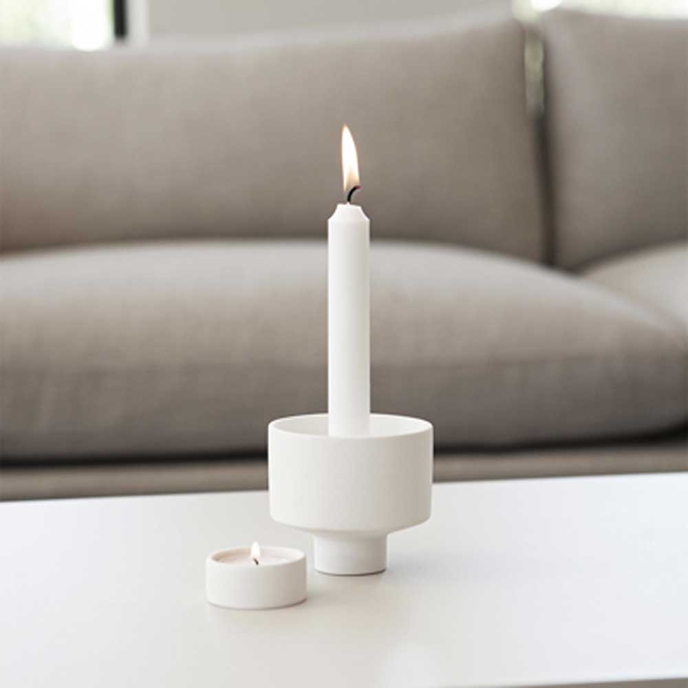 Ein Storefactory - Liaved Kerzenhalter für Stabkerzen und Teelicht weiß steht auf einem Tisch neben einer Couch.